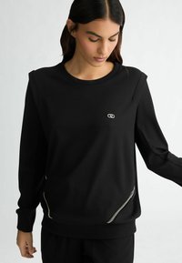 Felpa nera con collo a giro, maniche lunghe e dettagli in zip argentati di lato. Realizzata in un tessuto morbido e strutturato.