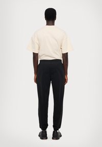 T-shirt crème à manches courtes associé à un pantalon noir ajusté, présenté de dos. Les chaussures présentent un design noir avec des accents colorés.