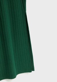 Jupe verte côtelée avec des plis verticaux, texture douce et une légère fente latérale à l'ourlet. Les bords sont finis par une couture nette.