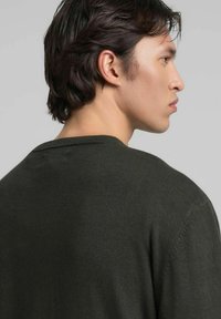 Donkergroene gebreide trui met een ronde hals en subtiele textuur. De achterkant wordt getoond, waarbij het zachte materiaal en de schoudernaden worden benadrukt.