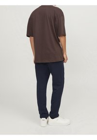 Brown oversized T-shirt paired with navy sweatpants. White sneakers complete the outfit. Fabric appears soft with a relaxed fit.