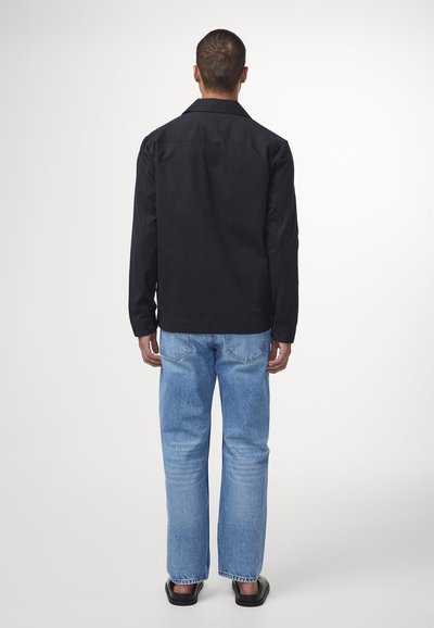 Zwarte katoenen shirt met een klassieke kraag, gecombineerd met lichtblauwe denim jeans. De jeans zijn iets losjes en hebben achterzakken.
