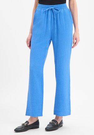 Pantalon bleu texturé à jambes droites avec taille élastique et cordon, porté avec des mocassins noirs et un top noir.