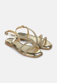 Sandali piatti in oro con cinturini incrociati, abbelliti con dettagli metallici e una punta quadrata. Finitura liscia e lucida in tutto.