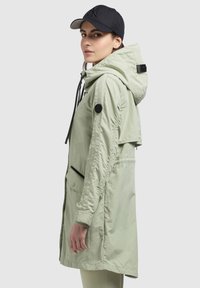 Šviesiai žalia, lengva parka su gobtuvu, juodais akcentais, priekinėmis kišenėmis ir raišteliu. Papildyta juodu kepurėle. Švelnus, elegantiškas dizainas.