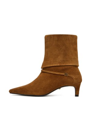 Stivaletto alla caviglia in camoscio marrone con punta appuntita, tacco basso a gattino, parte superiore morbida e dettaglio sottile con fibbia dorata piccola.
