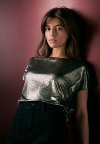 Metallisk mörkgrön topp med korta ärmar, slät textur, ledig passform, kombinerad med svarta högmidjade byxor med framfickor och knäppning.