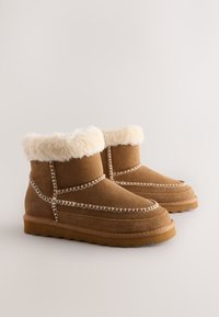 Bottes cheville en daim marron avec un revers en fausse fourrure, des coutures décoratives le long des coutures, et une semelle en caoutchouc texturée.