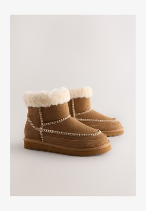 Brown suede ankle boots with a faux fur cuff, decorative stitching along the seams, and a textured rubber sole.