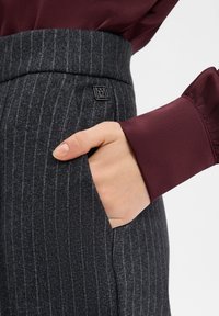 Gray striped trousers with a sleek waistband and pocket detail, paired with a burgundy satin blouse featuring puffy cuff accents.