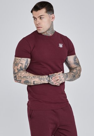 Camiseta de manga corta burdeos hecha de algodón, con un bordado de logo blanco en el pecho. Textura suave y diseño ajustado.