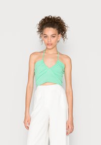Top cropped verde menta com decote em V e alças, apresentando tecido franzido na zona do busto e design minimalista. Combinado com calças largas brancas.