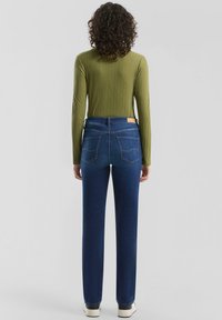 Zielony prążkowany top z długim rękawem w połączeniu z ciemnoniebieskimi, prostymi dżinsami. Dżinsy mają pięć kieszeni i brązową metkę na pasku.