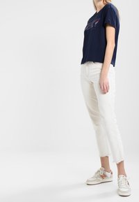 Navy cotton t-shirt with short sleeves and front graphic, paired with white cropped denim jeans and light gray sneakers with orange accents.