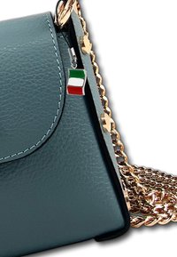 Sac en cuir bleu canard avec une bandoulière en chaîne dorée ; il dispose d'un petit charm en forme de drapeau italien attaché au rabat. Le coutures sont visibles le long des bords.
