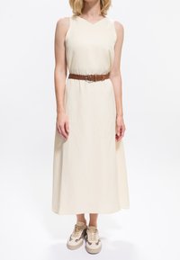 Kremowa, bezrękawnikowa sukienka midi z dekoltem w serek. Zdobiona brązowym plecionym paskiem z srebrną klamrą, zestawiona z beżowymi tenisówkami w panterkę.