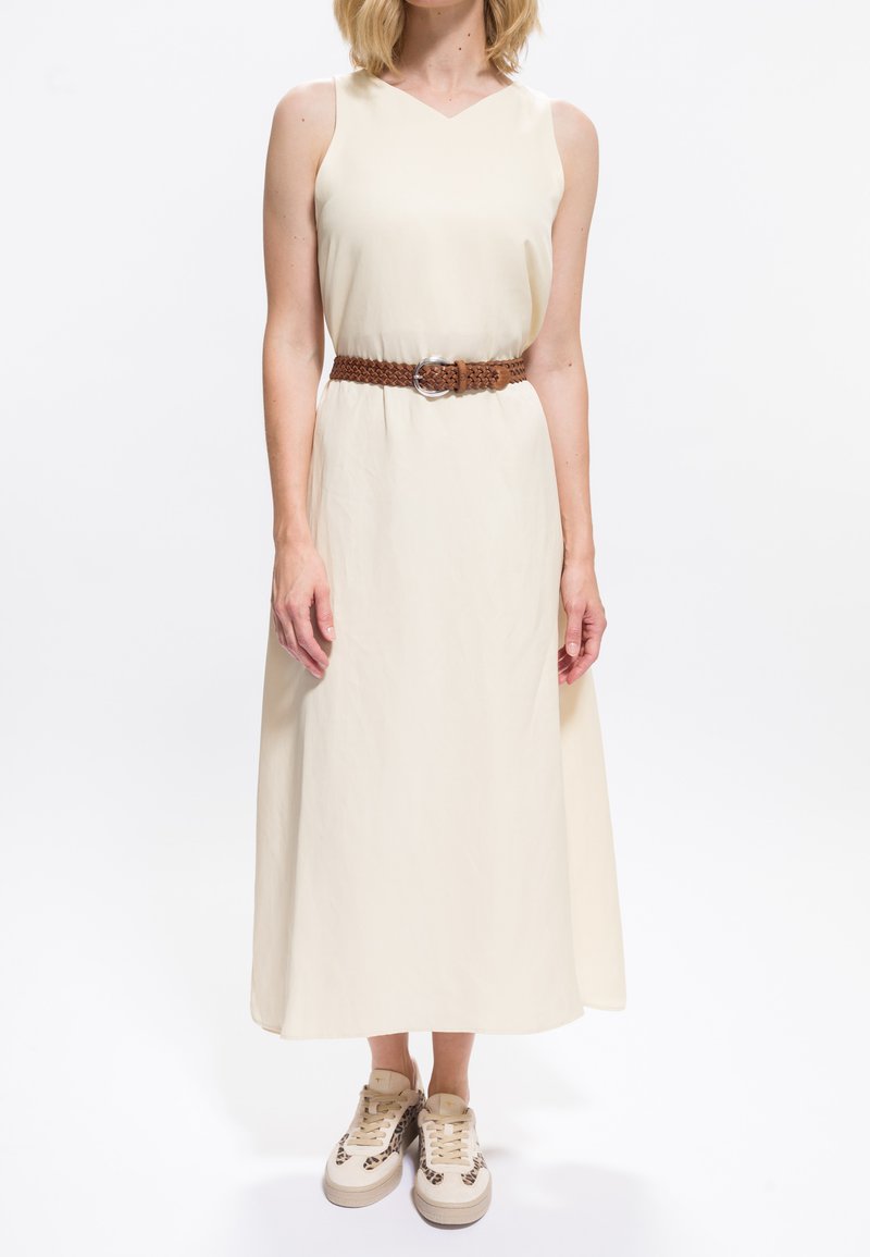 Kremowa, bezrękawnikowa sukienka midi z dekoltem w serek. Zdobiona brązowym plecionym paskiem z srebrną klamrą, zestawiona z beżowymi tenisówkami w panterkę.