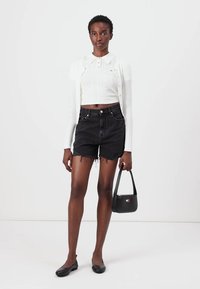 White ribbed cropped sweater with collar, black high-waisted denim shorts with frayed hem, and black flats. Holding a small black handbag.