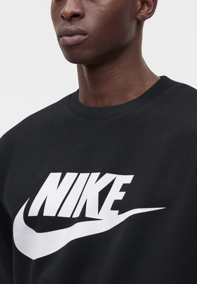 Primer plano de una persona que lleva una sudadera negra con un gran logo blanco de Nike en el pecho.