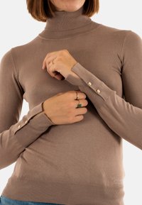 Beige Rollkragenpullover aus geripptem Strickstoff, mit Knöpfen an den Handgelenkabschlüssen und einer taillierten Silhouette mit nahtlosem Design.