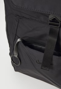 Zwarte nylon rugtas met een voorvak met rits, verstelbare band, ronde hardware en subtiele merklogo-details.