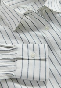 Camisa blanca abotonada con finas rayas verticales negras, que presenta un cuello y un puño abotonado.
