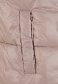 Kurtka puchowa w jasnym beżu, wykonana z gładkiego, błyszczącego materiału. Posiada poziomy wzór przeszyć oraz kieszeń na łatkę.