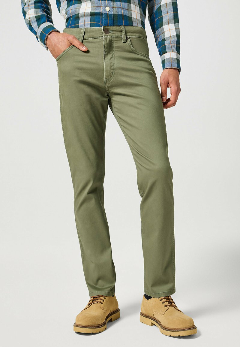Pantalones de algodón verdes con un diseño ajustado, que cuentan con bolsillos delanteros y costuras en contraste, combinados con botas marrones y una camisa de cuadros.