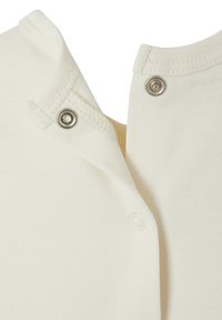 Nahaufnahme von cremefarbenem Stoff mit teilweise befestigten Druckknöpfen aus Metall, die Nähte und die weiche Textur zeigen.