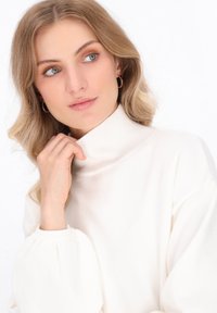 Crème turtleneck trui gemaakt van zacht breimateriaal, met een geribde kraag en volumineuze ballonmouwen, aangevuld met een gladde textuur.