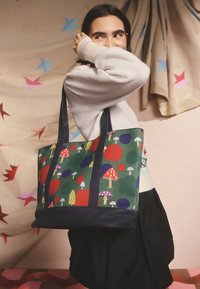 Kangaskassi, jonka taustaväri on vihreä ja jossa on värikkäitä sieni- ja pallokuvioita. Siinä on tummansiniset hihnat ja jämäkkä suorakaiteen muotoinen rakenne.