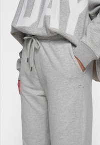 Lichtgrijze joggingsbroek met zijzakken, een elastische tailleband met een trekkoord en ribgebreide boorden. De stof is zacht en gestructureerd.