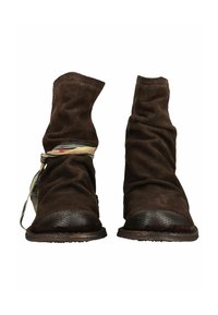 Paire de bottes en cuir souple marron foncé usées, l'une avec un ruban en tissu rayé enroulé autour de la cheville, vue de face sur fond blanc.