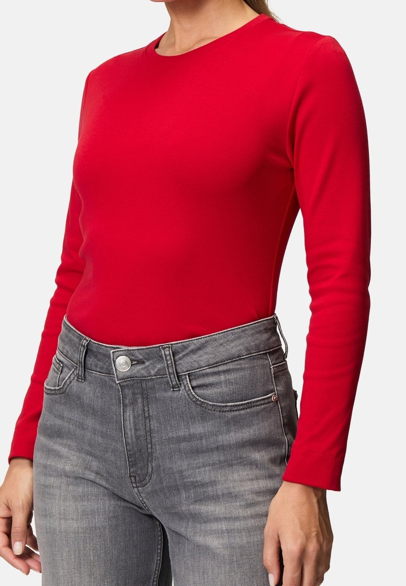 Rotes Langarmoberteil aus weichem Stoff, taillierte Passform, runder Ausschnitt, getragen mit hochgeschnittenen grauen Jeans mit fünf Taschen und Knopfverschluss.