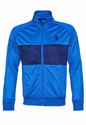 Veste de sport bleue zippée avec une bande horizontale bleu marine foncé sur la poitrine et un petit logo sur la partie gauche de la poitrine.