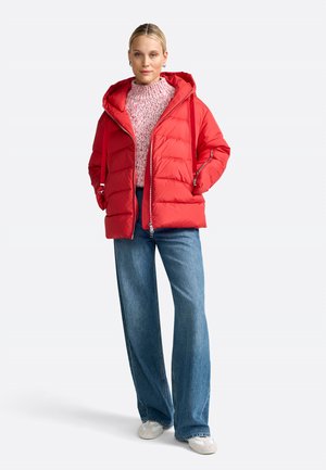 Rdeča puhasta jakna s kapuco, z vodoravnim šivom, sprednjim zadrgo in sproščenim krojem, v kombinaciji s svetlo modrimi širokimi hlačami.