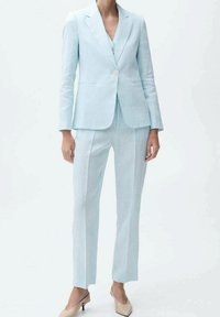 Costume en lin bleu clair avec une veste ajustée et un pantalon droit. Présente des textures subtiles et une fermeture à un bouton sur la veste.