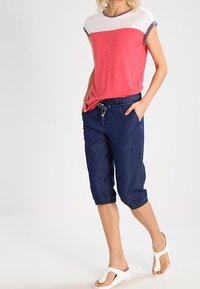 Červeno-bílý tričko s krátkým rukávem a barevným blokováním, spárované s námořnickými zkrácenými kalhotami s elastickým pasem a bočními kapsami. Bílé sandály.