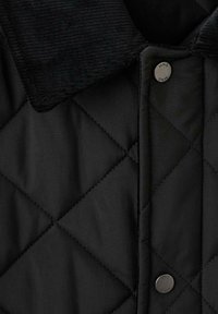 Giacca trapuntata nera con colletto in velluto a coste nero, dotata di chiusura con bottoni a pressione e texture a motivo a diamante sul tessuto.