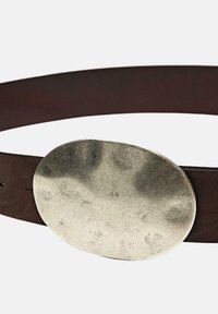 Bruine leren riem met een grote, ovale, geborsteld zilveren metalen gesp met een licht gestructureerde afwerking en minimale hardwaredetails.