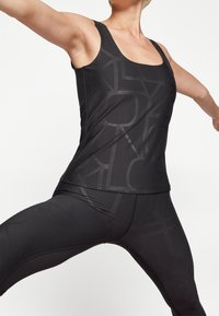 Černý sportovní top s hladkou texturou a velkým geometrickým vzorem. Spárovaný s odpovídajícími černými legínami, oba navržené pro aktivní nošení.