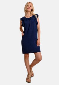 Abito blu navy con maniche a sbuffo, vestibilità rilassata, lunghezza al ginocchio, realizzato in tessuto leggero. Indossato con sandali beige con cinturini.