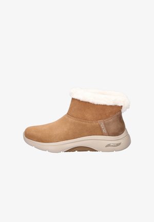 Bruine suède enkelboots met een faux fur voering, ronde neus en beige rubberen zool. Heeft een metalen accent aan de zijkant.