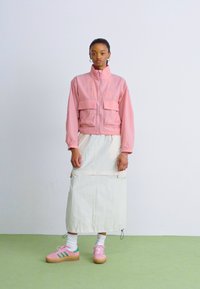 Rosa lett jakke med to frontlommer, parret med en kremfarget midi-skjørt og pastellrosa sneakers med grønne detaljer.