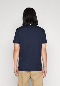 Marineblauwe polo met korte mouwen, gemaakt van katoen. Heeft een klassieke kraag, subtiele textuur en een kleine rode accentkleur bij de hals.