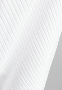 Närbild av vit ribbad tyg med diagonala veck och mjuk textur mot en ljusgrå bakgrund.