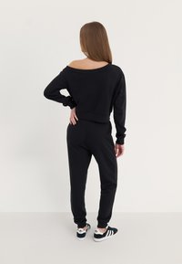 Sweatshirt noir court avec design décolleté, associé à un jogging noir. Le sweatshirt présente des poignets côtelés ; le jogging a une taille élastique.