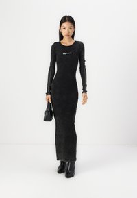 Svart långärmad klänning med en figursydd silhuett, gjord av texturerad tyg, med en logotyp på bröstet och en hög halsringning.