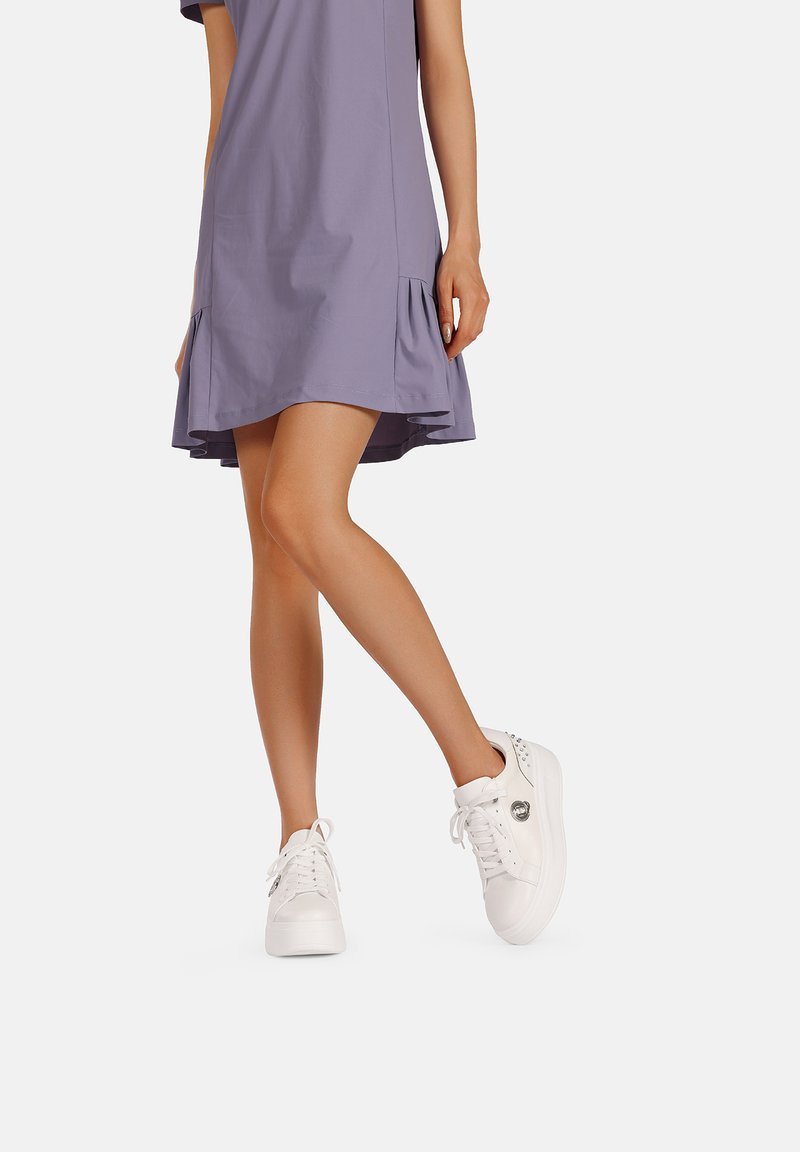 Sneakers bianchi con una texture liscia, punta rotonda e design con lacci. Abbinati a un vestito lavanda con un orlo svasato e pieghe decorative.