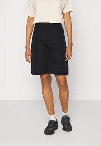 Černé cargo šortky se bočními kapsami, délka ke kolenům, vyrobené z lehkého materiálu. V kombinaci s béžovým tričkem a černými teniskami.